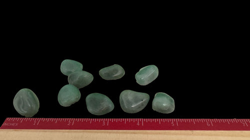 Handful of tumbled green aventurine stones on a black surface with a ruler for size reference.